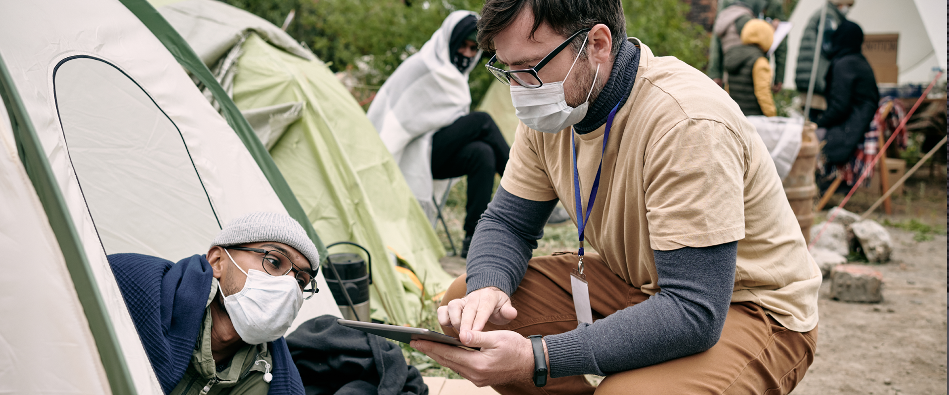 Photo illustrating the International Crisis Response Association's focus, a team of workers are shown sitting around a campsite with someone in the foreground consulting a tablet.