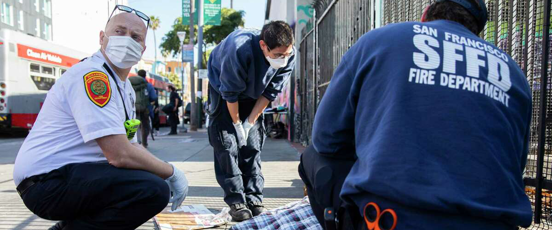 Photo illustrating the International Crisis Response Association's focus: San Franscisco Crisis Response Team fire department, medic, and social worker team check on a person shown only as legs under a sleeping bag on a city street.